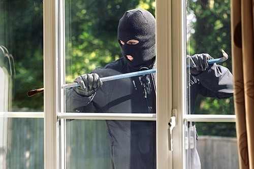 Einbrecher mit Brecheisen vor Fenster
